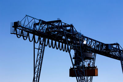 Low angle view of crane at construction site against clear sky