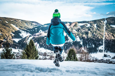 Rear view of boy jumping on snowfield against mountains