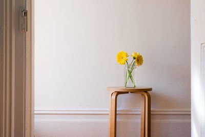 Yellow flowers in vase against wall at home