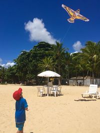 Low angle view of boy flying kite against blue sky