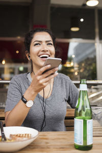 Happy woman using mobile phone while sitting at sidewalk cafe