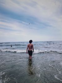 Rear view of shirtless man on beach against sky