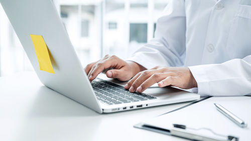 Midsection of doctor using laptop at clinic