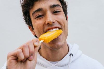 Happy young male eating sweet orange ice lolly enjoying taste on white background