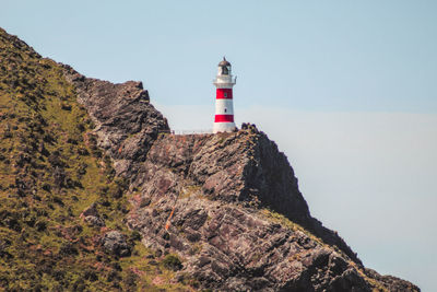 Lighthouse on rock by building against sky