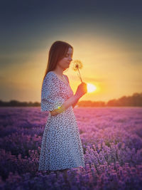 Rear view of young woman standing against sky during sunset