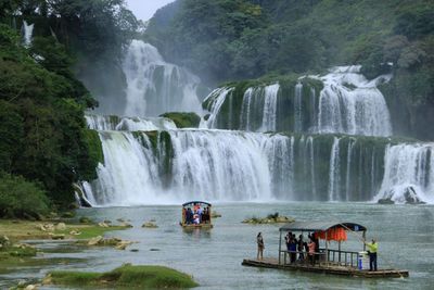 People on wooden craft moving towards waterfall in forest