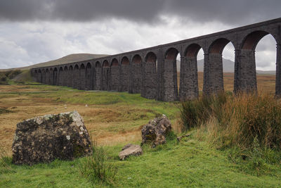 Arch bridge on field against sky