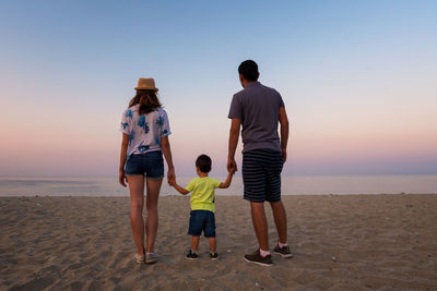 Rear view of cheerful family standing at beach during sunset