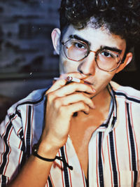 Close-up portrait of young man wearing eyeglasses smoking cigarette