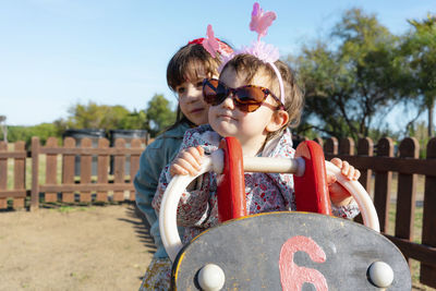 Sisters sitting on motorcycle at playground during sunny day