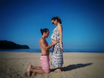 Father and son sitting on beach against clear blue sky