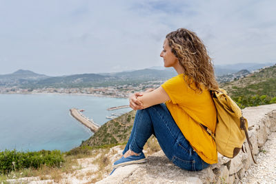 Young woman sitting on shore against mountains