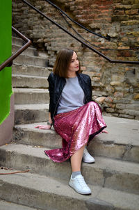 Full length of thoughtful woman sitting on steps against wall