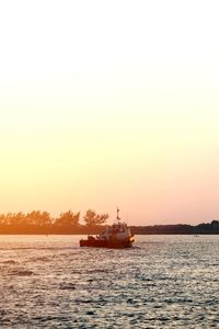 Silhouette boat sailing in sea against clear sky during sunset