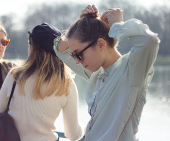 Young woman tying hair bun while standing with friends at lakeshore