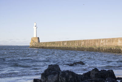 Lighthouse by sea against clear sky