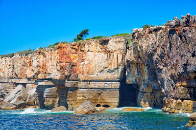 Rock formations by sea against clear blue sky