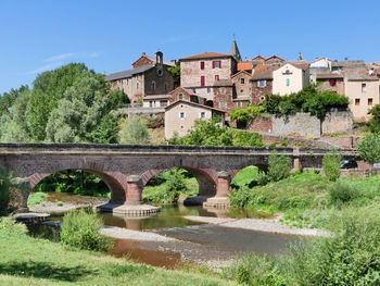 Arch bridge over river by buildings against sky