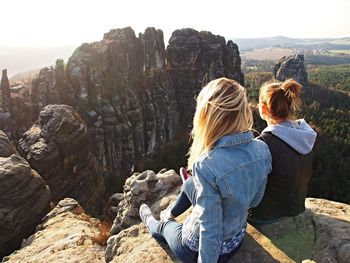 Rear view of female friends sitting on cliff against rock formations
