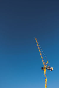 Low angle view of crane against clear blue sky