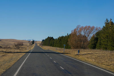 Road amidst trees against clear blue sky