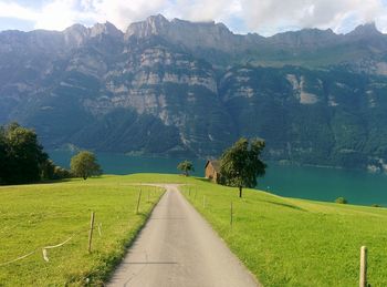 Empty road amidst grassy field by walensee against swiss alps