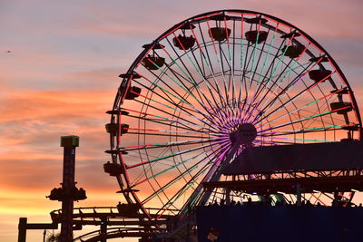 Amusement park rides against cloudy sky during sunset