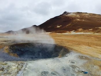 Steam coming out from geyser against cloudy sky