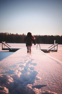 Rear view of girl running on snow covered pier