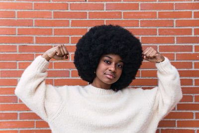 Portrait of young woman standing against brick wall
