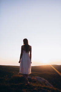 Rear view of young woman standing at field against clear sky
