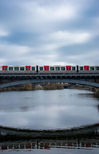 Train on railway bridge over river against cloudy sky