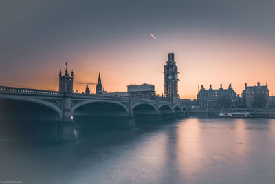 Bridge over river in city against sky during sunset