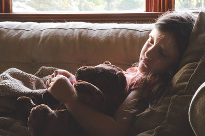 Girl sleeping with teddy bear on sofa at home