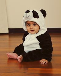 Baby boy wearing warm clothing while sitting on hardwood floor