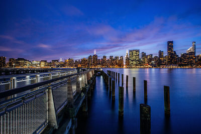 Illuminated buildings by river against sky at night