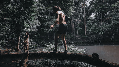 Full length of shirtless man standing by tree in forest