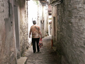Rear view of senior woman walking on alley amidst old buildings