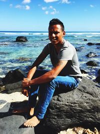 Portrait of smiling man sitting on rock at beach