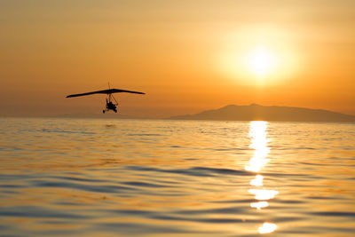 Silhouette hang glider over sea against clear sky during sunset