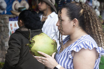 Latin young woman drinking coconut water in the market
