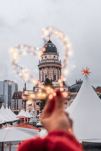 Low angle view of hand holding illuminated building against sky