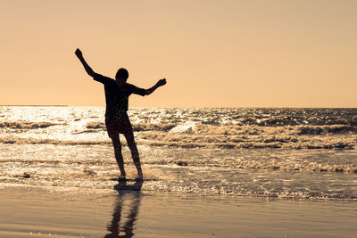 Man standing in sea against clear sky during sunset