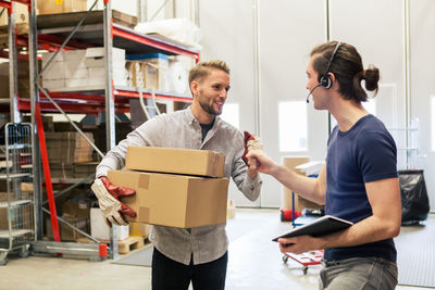 Male colleagues discussing over digital tablet and cardboard boxes at industry