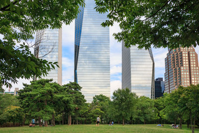 People in park by modern buildings in city against sky