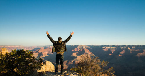 Rear view of person standing next to mountains against clear sky