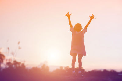 Rear view of woman standing on field against sky during sunset