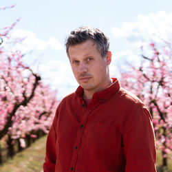 Portrait of a man in a red shirt in a field of flowering peach trees in aitona, catalonia, spain.