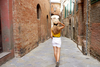 Back view of beautiful tourist girl walking between narrow alleys of siena historic town of tuscany,